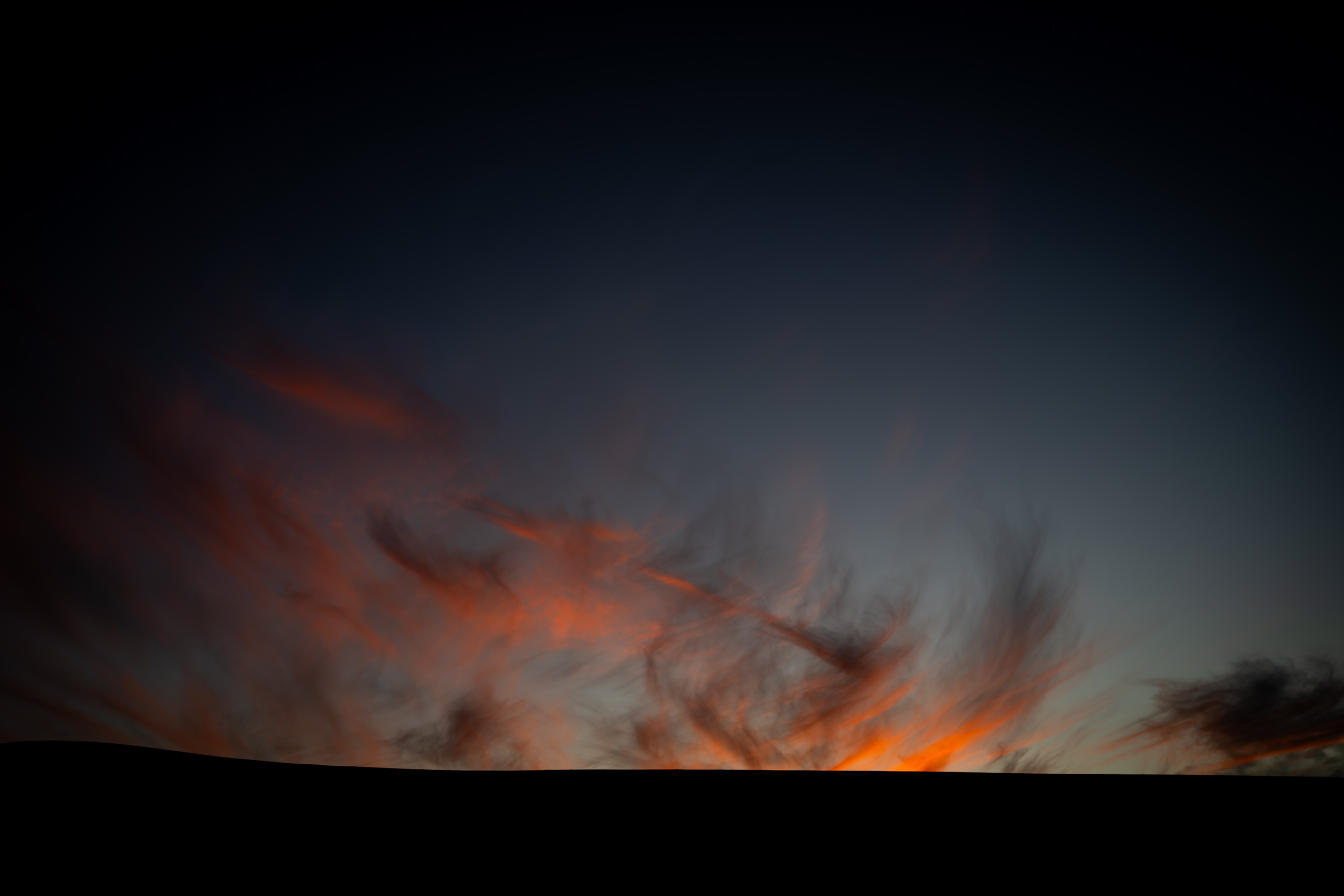 Un ciel sombre traversé de longues traînées orange, au-dessus d'une ligne d'horizon entièrement noire.